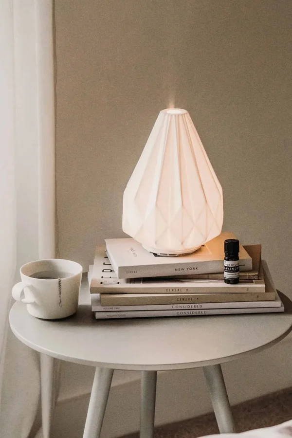 Ceramiczny dyfuzor na stosie książek i filiżanka z herbatą na minimalistycznym stoliku